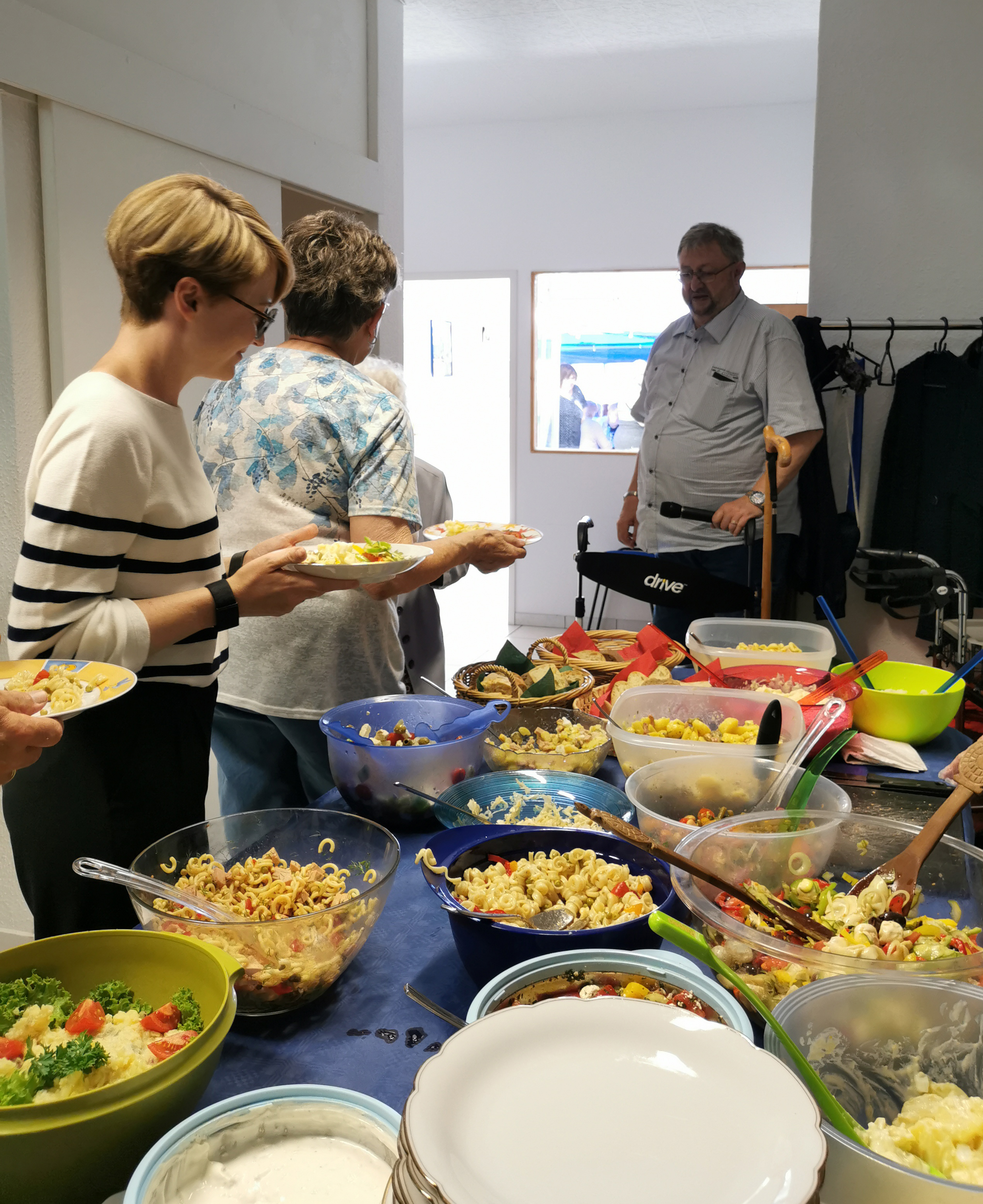 Zwei Mitglieder stehen mit Tellern am Salatbuffet, im Hintergrund ist Ortsverbands-Vorsitzender Jürgen Wöhrle zu sehen.