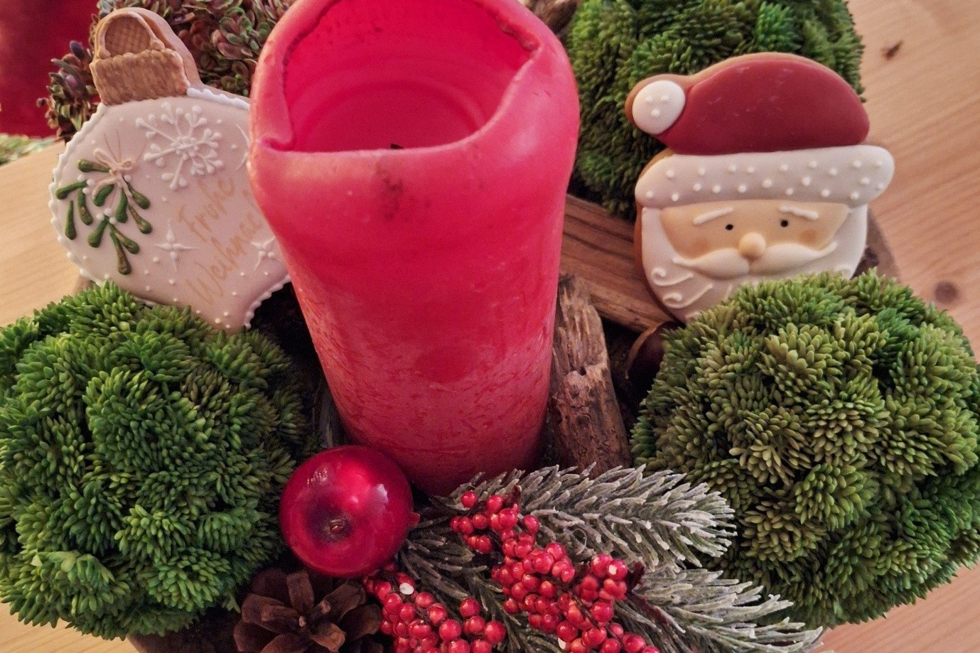 Weihnachtsgesteck Ein weihnachtsgesteck mit roter Kerze, Tanne, Keks-Weihnachtsmanngesicht, Keks-Tannenbaumkugel in weiß und grüne Pflanzenkugeln