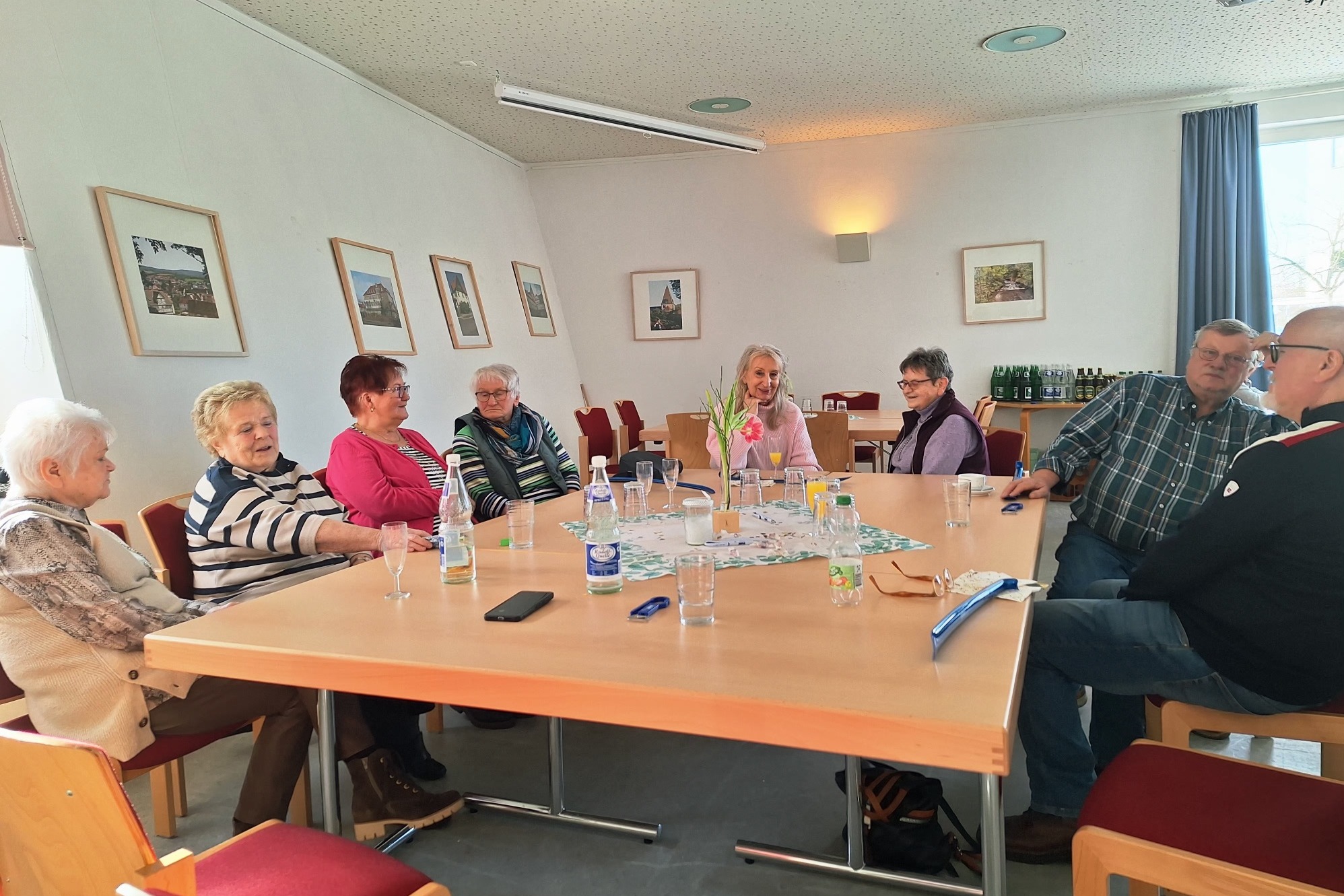 Ein Raum mit mehreren Tischen an denen G&auml;ste, meist &auml;lteren Menschen sitzen, sie haben Getr&auml;nke auf den Tischen stehen und unterhalten sich.