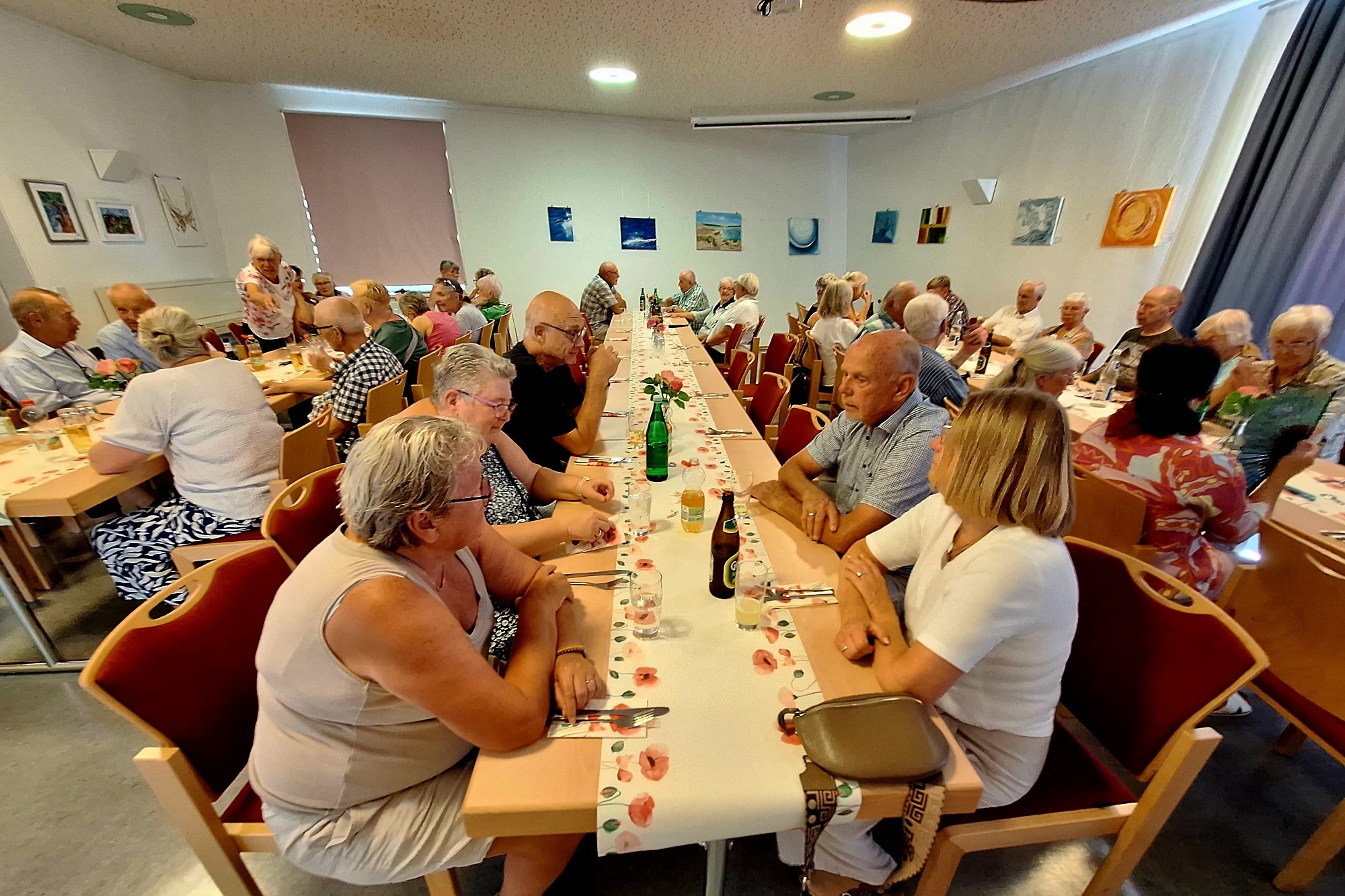 Ein kleinerer Saal mit ca. 50 Menschen an 3 Tischreihen